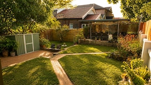 Un jardin avec un chemin en briques, des plantes en pot et du mobilier d’extérieur.