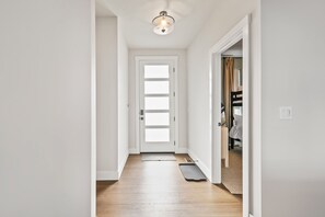 Un couloir avec une porte blanche, un luminaire au plafond et un paillasson.