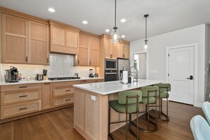 Une cuisine moderne avec des meubles en bois, un îlot central, des tabourets de bar et des luminaires suspendus.