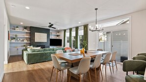 A modern living room with a dining area, wooden flooring, green sofa, and a flat-screen TV mounted on the wall. - Pro Golf Simulator and Hot Tub, New Luxury 4 BR, Boise Home Sleeps 12 (Boise)