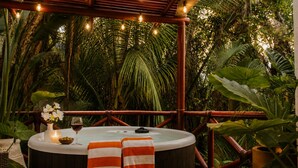 Un jacuzzi con toallas a rayas, una vela y una copa de vino sobre una mesa rodeada de exuberante vegetación.