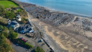 An aerial view of a coastal area with houses, a parking lot, and a rocky shoreline. - Puffin Lodge - 2 Bedroom Lodge - Wisemans Bridge (Kilgetty)