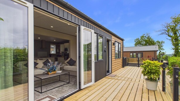 A modern mobile home with a deck, sliding glass doors, and a visible kitchen area. - Puffin Lodge - 2 Bedroom Lodge - Wisemans Bridge (Kilgetty)
