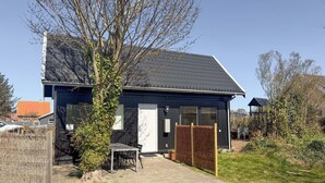 Una casa moderna amb façana fosca, teulat de rajola i pati pavimentat amb taula i cadires.