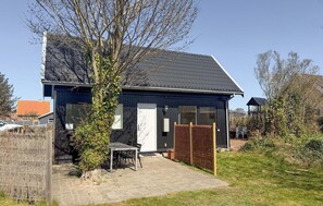 A modern house with a dark exterior, a tiled roof, and a paved patio area with a table and chairs.