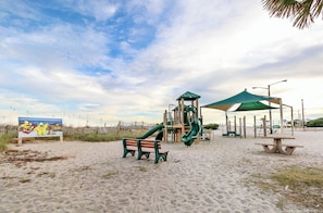 Ein Spielplatz am Strand mit Rutsche, Bänken und einem Picknicktisch.