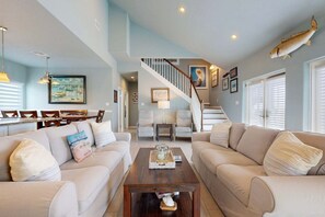 A spacious living room with a sofa set, a coffee table, and a staircase leading to an upper level. - LCV33 Shared Pool, Private Hot Tub,Propane Grill (Port Aransas)