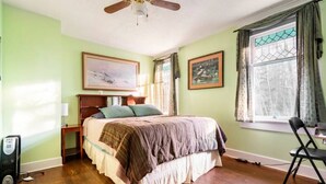 A bedroom with a bed, a ceiling fan, a window with curtains, and a chair.