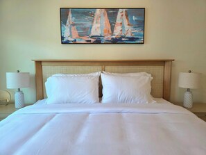 Un lit bien fait, avec du linge de lit blanc, une tête de lit ornée d’un motif tissé et deux lampes de chevet à abat-jour blanc.