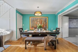 A dining room with a wooden table set for four, a bench, and a large painting on the wall. - Spacious 4 Bedroom Home Near Bowness Park 🌿 (Calgary)