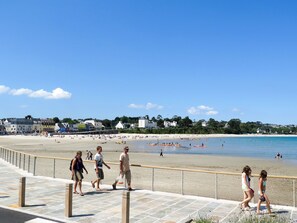 Eine Strandpromenade mit einem Pflasterweg, einem Metallgeländer und Blick auf den Strand und das Meer.