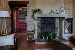 Una sala de estar acogedora con chimenea, una estantería, una cesta de mimbre y una lámpara.