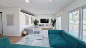 A modern living room with a sectional sofa, a flat-screen TV, and a large window. - Serene Modern Luxe king Suite~Minutes To Lido Beach, Downtown, UTC + Siesta Key (Sarasota)