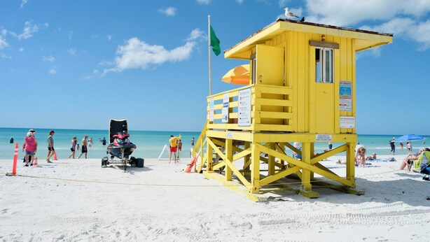 A lifeguard tower with a flag, a lifeguard chair, and a beach umbrella. - Serene Modern Luxe king Suite~Minutes To Lido Beach, Downtown, UTC + Siesta Key (Sarasota)