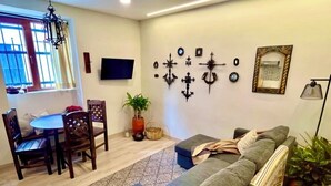Ein Wohnzimmer mit einer Couch, einem Esstisch, Stühlen, einem Fernseher, Wanddekoration und einer Zimmerpflanze.