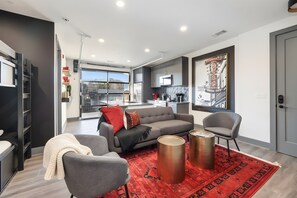 Ein modernes Wohnzimmer mit einem grauen Sofa, einem roten Teppich und zwei metallischen Beistelltischen.