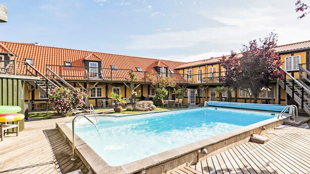 En swimmingpool med ett trädäck, en täckt uteplats och en byggnad med ett tak täckt av tegelpannor.