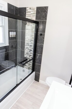 Et moderne badeværelse med bruseniche, hvidt toilet og flisegulv.