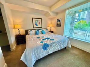 A bedroom with a bed, two bedside lamps, a window with blinds, and two framed pictures on the wall. - Chic & Modern 2BR Condo (Salt Lake City)