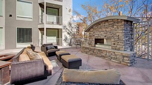 A patio with wicker furniture, a stone fireplace, and a view of a multi-story building. - Chic & Modern 2BR Condo (Salt Lake City)