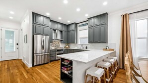 Una cocina moderna con armarios grises, electrodomésticos de acero inoxidable y una isla central con taburetes de bar.