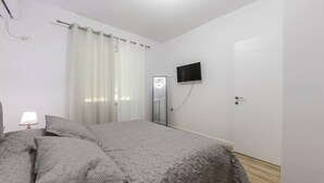 Un dormitorio con cama, cortinas, televisor y puerta.