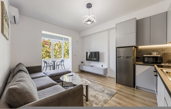 Un espacio de estar moderno con sofá, mesa de centro, televisor, zona de cocina y mesa de comedor con sillas.