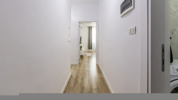 A hallway with a wooden floor, white walls, a door on the right, and a framed picture above it. - Casa Tirana Cozy 2BR Apartment Near Main Square (Tirana)