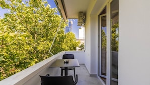 A balcony with a table and chairs, a view of trees, and a building in the background. - Casa Tirana Cozy 2BR Apartment Near Main Square (Tirana)