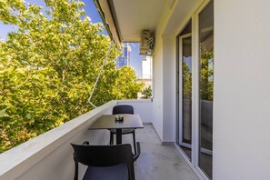 A balcony with a table and chairs, a view of trees, and a building in the background. - Casa Tirana Cozy 2BR Apartment Near Main Square (Tirana)