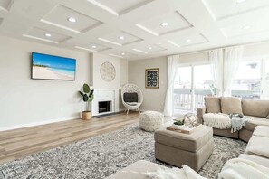 Ein modernes Wohnzimmer mit Kamin, einer Sofagarnitur, einem großen Teppich und Blick ins Freie.