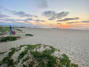 Ein Strand mit einem Steg im Hintergrund und einem Sonnenuntergang.