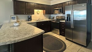 A modern kitchen with dark cabinetry, stainless steel appliances, a granite countertop, and a built-in island with bar stools. - Surfwatch II 204 - Oceanfront in Surfside Beach (Surfside Beach)