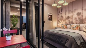 Ein Schlafzimmer mit einem Bett, einem roten Tisch mit Stühlen, einer Topfpflanze und einer Wand mit Blumenmuster.