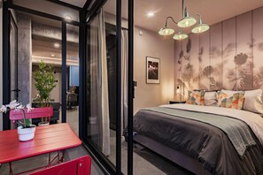 A bedroom with a bed, a red table with chairs, a potted plant, and a wall with a floral pattern. - Private Balcony with Garden & Gym Access (Mexico City)