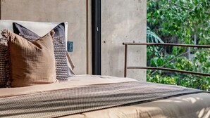 Un dormitorio con una cama grande, vistas a la vegetación a través de una ventana y una pared de concreto.