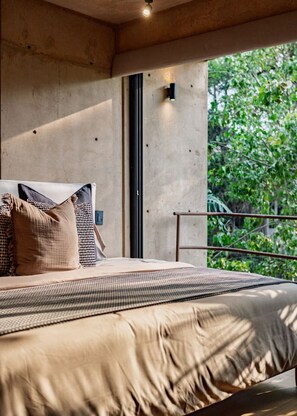 Un dormitorio con una cama grande, vistas a la vegetación a través de una ventana y una pared de concreto.