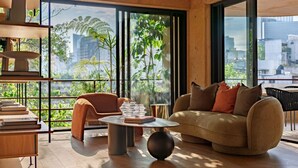 Una sala de estar moderna con sofá, mesa de centro y estanterías, ventanas amplias con vista a la ciudad.