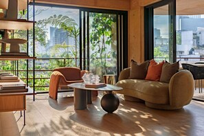 Una sala de estar moderna con sofá, mesa de centro y estanterías, ventanas amplias con vista a la ciudad.