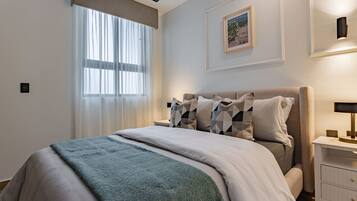 A bedroom with a bed, a nightstand, a lamp, a window with curtains, and a framed picture on the wall.