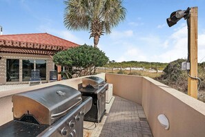 Eine Außenpatio mit Grill, ein Poolbereich und Blick auf den Strand.