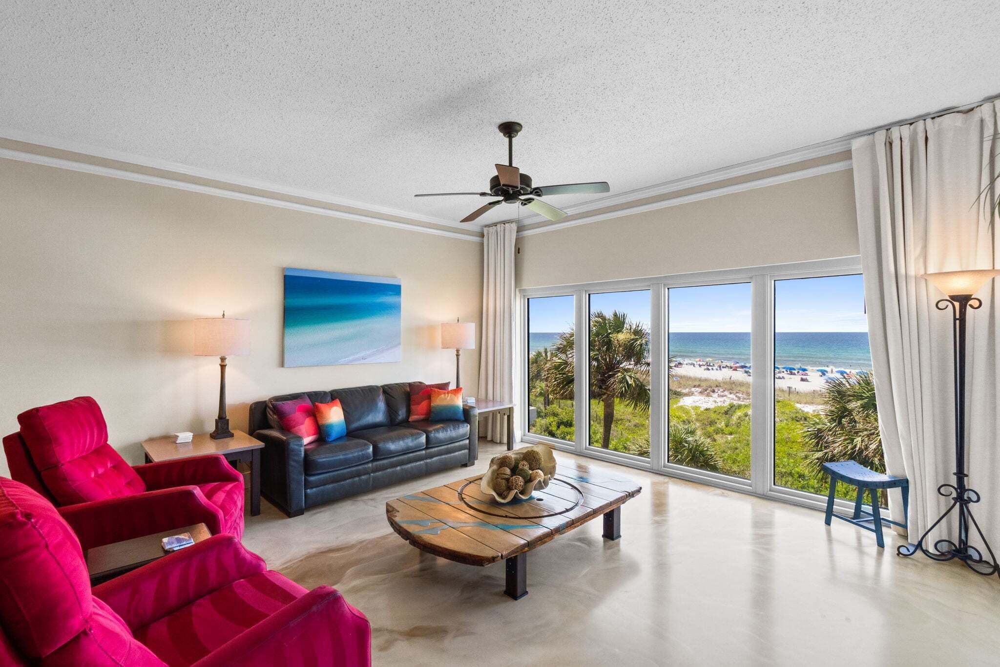 Ein großzügiger Wohnraum mit einem großen Fenster und Blick auf den Strand, einem Deckenventilator und einem modernen Couchtisch.