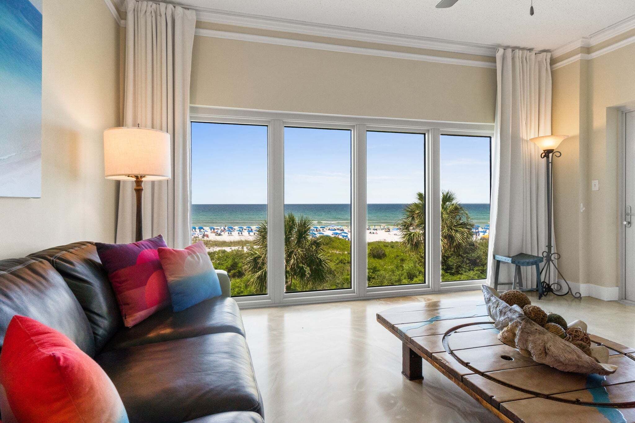 A living room with a large window overlooking a beach, a leather sofa, and a coffee table with decorative items.