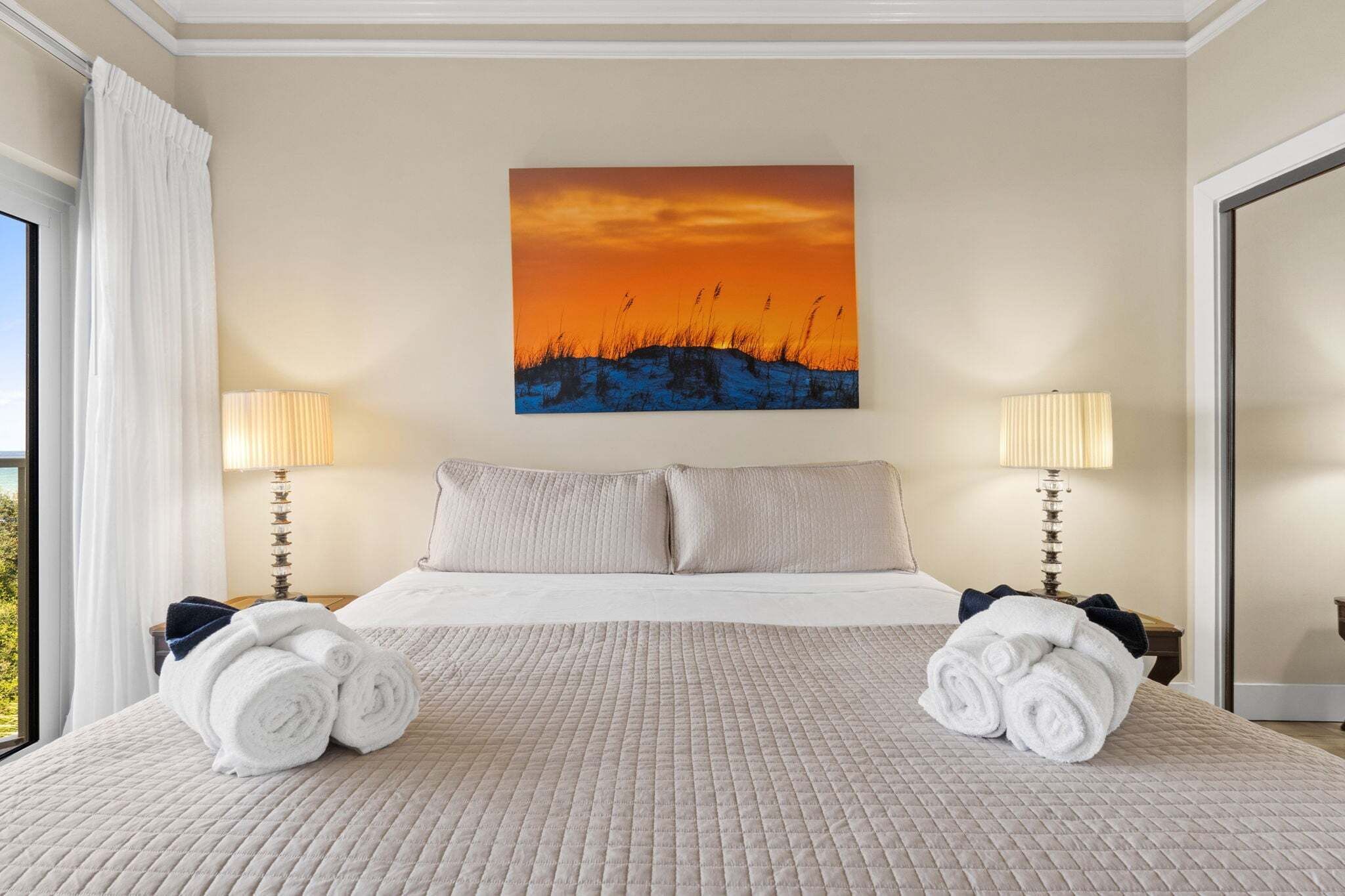 Ein Hotelzimmer mit einem Bett, zwei Nachttischlampen, einem Bild an der Wand und zusammengerollten Handtüchern auf dem Bett.
