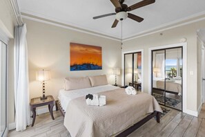 Une chambre d’hôtel avec un lit, deux lampes de chevet, un ventilateur de plafond, un tableau et une vue sur l’extérieur, accessible par une porte coulissante.