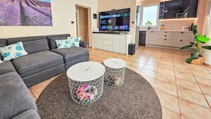 Un soggiorno moderno con un divano grigio, una televisione a schermo piatto e un angolo cottura con una finestra.