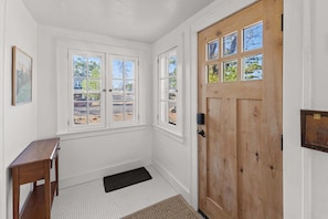A hallway with a wooden door, a bench, and a window with a view of a parking lot.