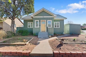 A two-story house with a front porch, a small garden, and a brick pathway leading to the door.