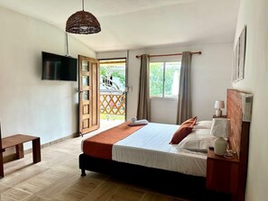 Ein Schlafzimmer mit Bett, Fernseher, Nachttisch mit Lampe, einer Holzbank und Blick ins Freie.