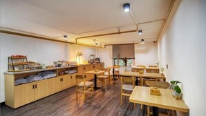 A dining area with wooden tables and chairs, a buffet counter, and a large window providing natural light. - Gongxili - Yuejian Hotel (Kunming)